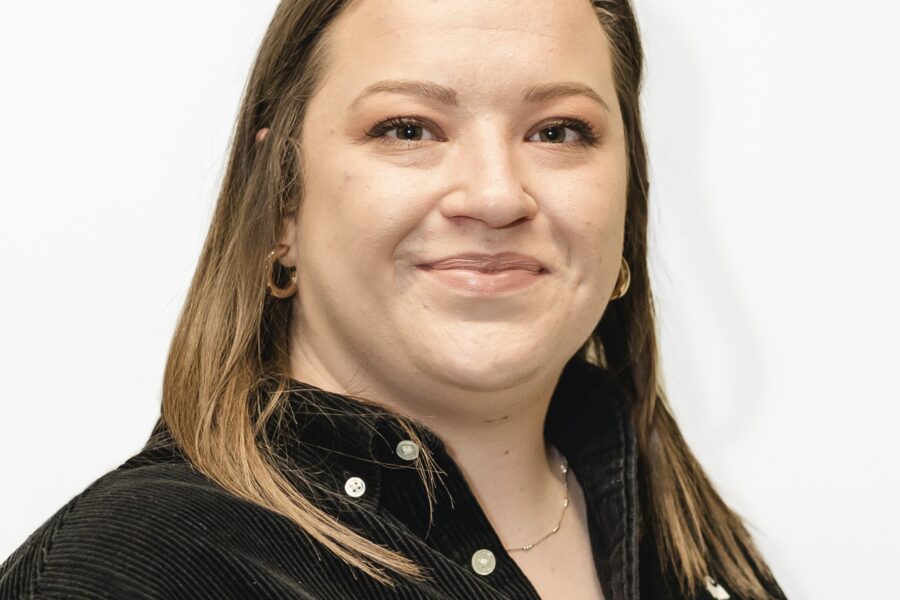 Charlotte facing towards the camera and smiling. She is standing against a white background