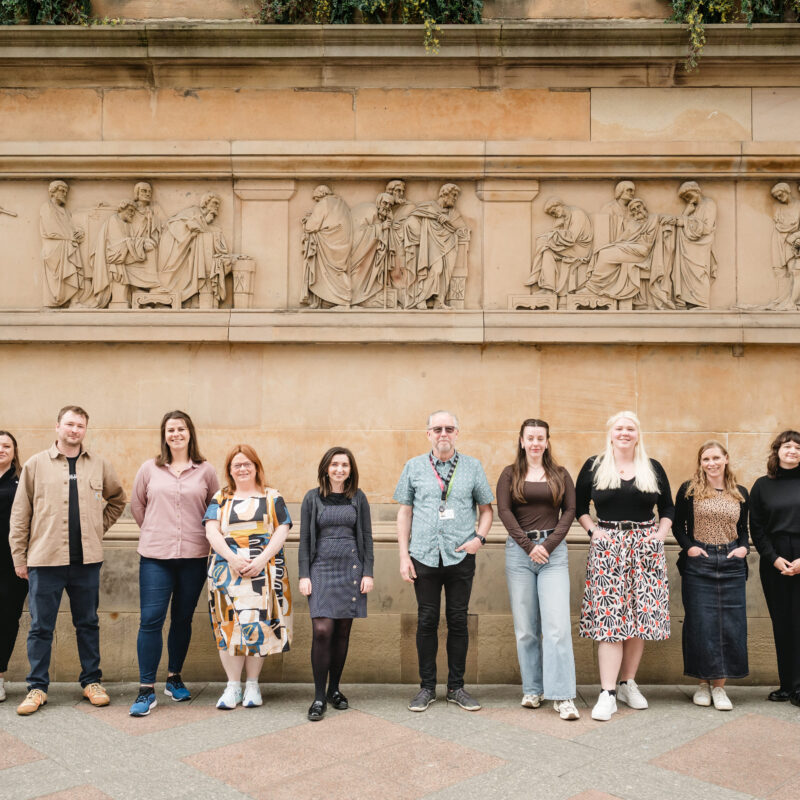 Heritage Network staff team standing in a line and facing the camera in front of a heritage building.