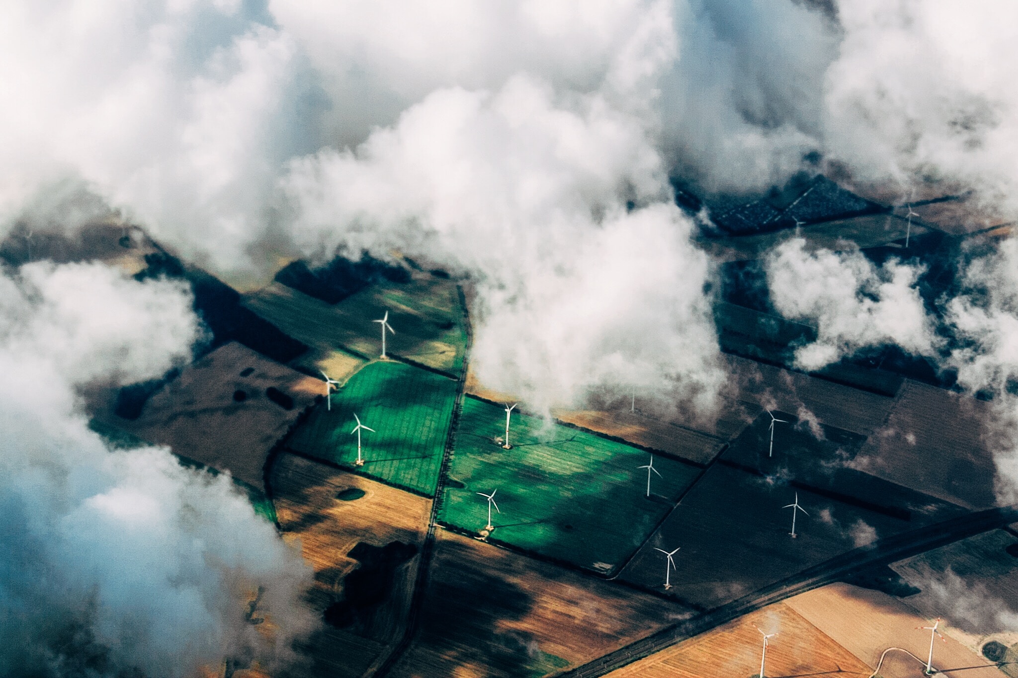 Aerial view of windmills in a green field surrounded by clouds.