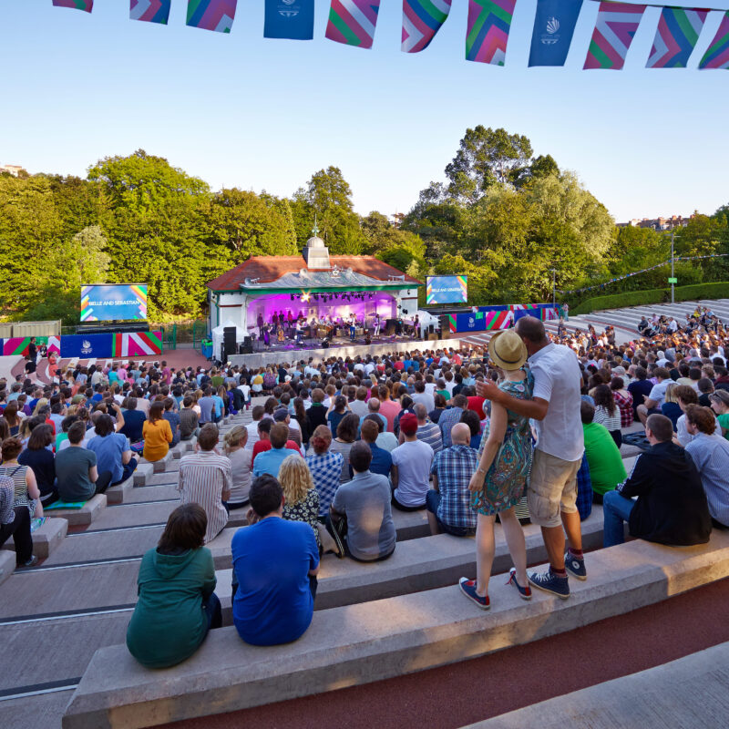 A crowd of people sitting and watching a performance at Kelvingrove Bandstand