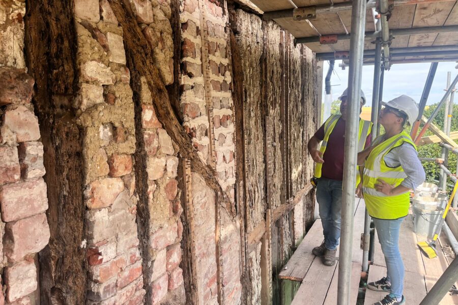 Two people in hi-viz jackets and hard hats stand on scaffolding inspecting the exposed bricks and timber of the chapel.