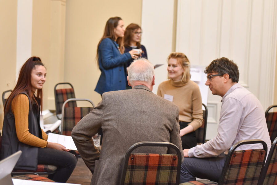 A group of people of mixed ages and genders sit in a small circle of chairs having a discussion.