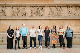 Nine Heritage Newtwork trustees in front of a stone building with a frieze