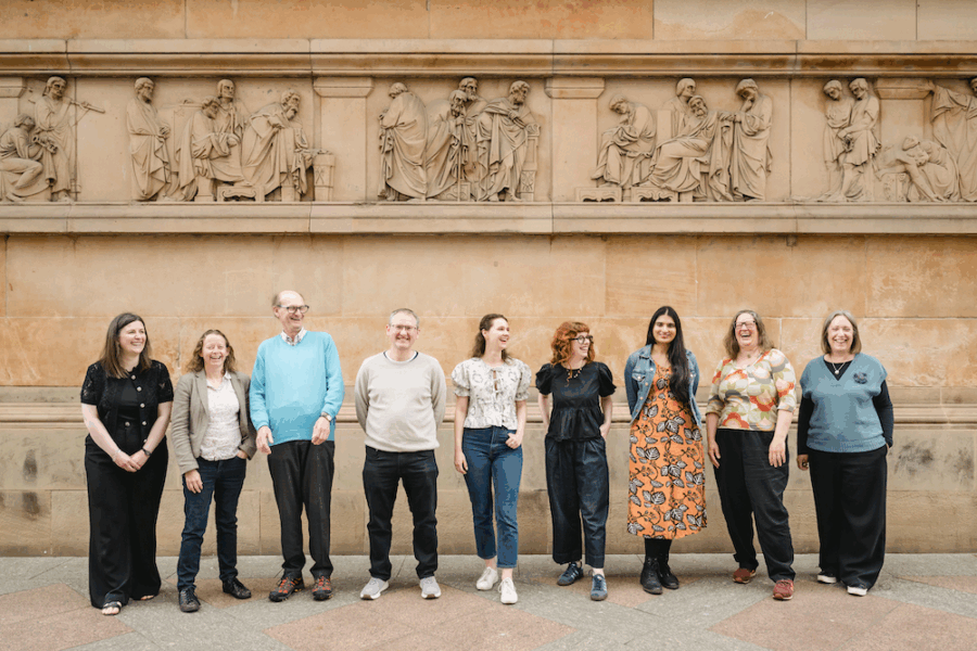 Nine Heritage Network trustees stood in front of a historic stone building with a frieze