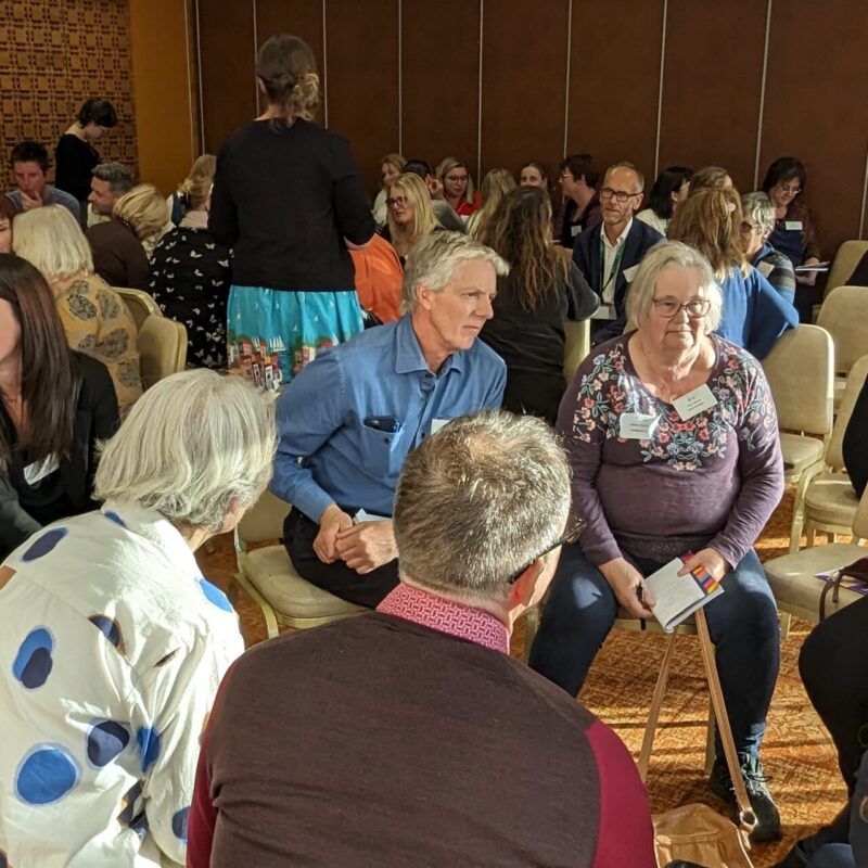 Groups of people sit together in circles at a conference, they are talking and interacting with each other.