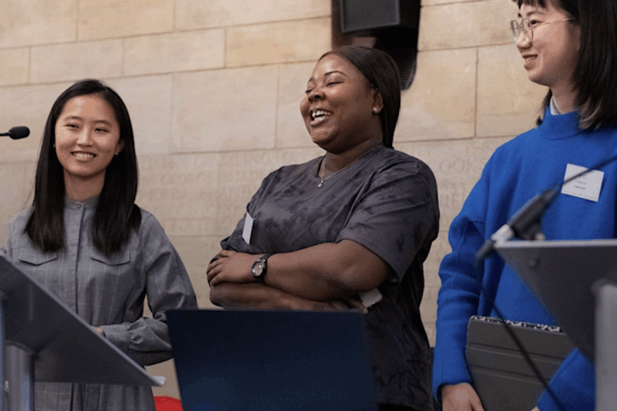three young people stand on a stage behind a podium, they are smiling and giving a speech