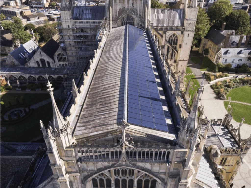 Alt text: An aerial photo looking down along the roof on a historic church. One side of the roof is covered by an array of solar panels.