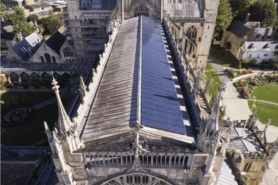 Alt text: An aerial photo looking down along the roof on a historic church. One side of the roof is covered by an array of solar panels.