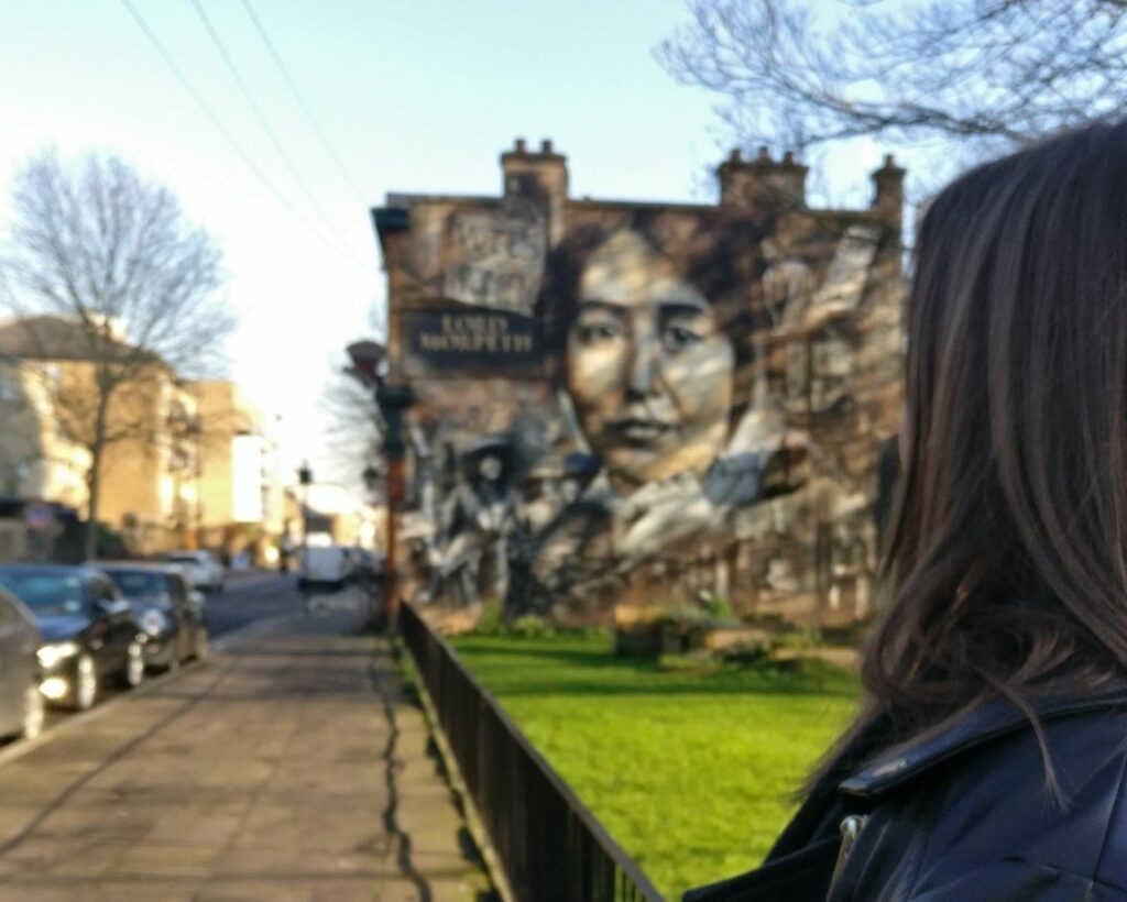 A woman is seen looking towards a mural of Sylvia Pankhurst on the side of a building in East London.