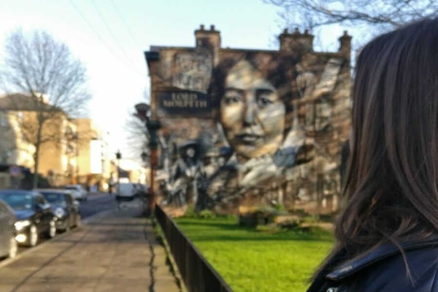 A woman is seen looking towards a mural of Sylvia Pankhurst on the side of a building in East London.