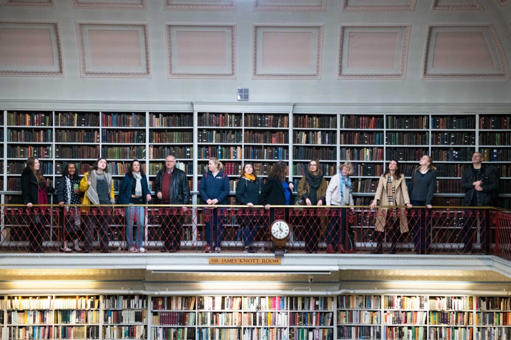 A group of people stood looking in various directions on a balcony in a library.