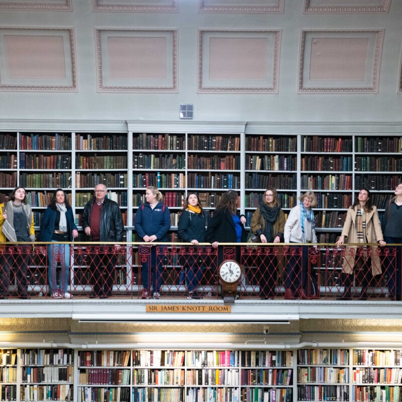 A group of people stood looking in various directions on a balcony in a library.