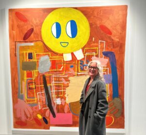 A blonde haired women standing in front of a orange mural smiling