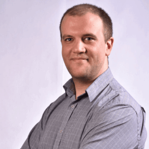 A man in a grey check shirt smiling at the camera