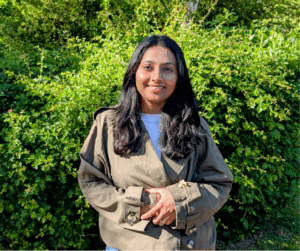 Woman against a green hedge smiling at the camera