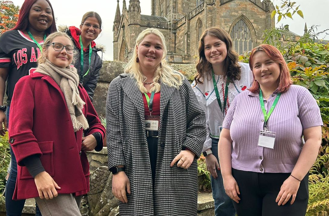 A group of 6 young people standing in a garden in front of Dunfermline Abbey on a sunny day
