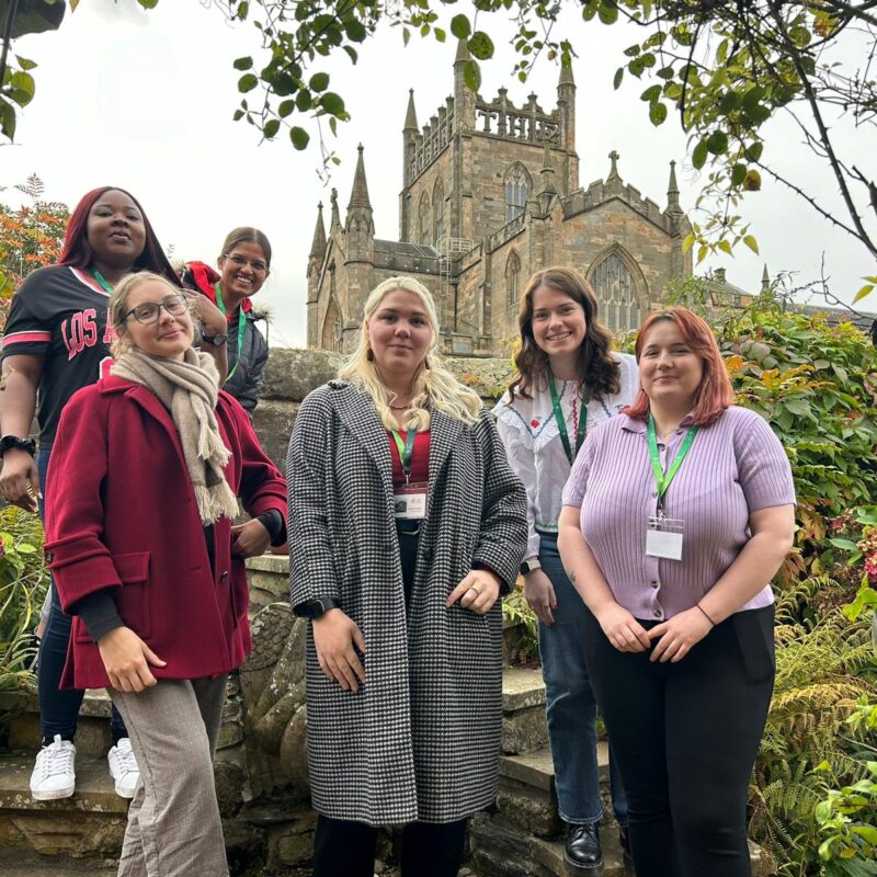 6 young people in a garden, smiling and facing the camera in front of Dunfermline Abbey