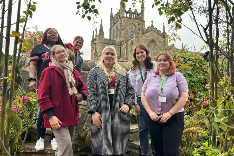 6 young people in a garden, smiling and facing the camera in front of Dunfermline Abbey