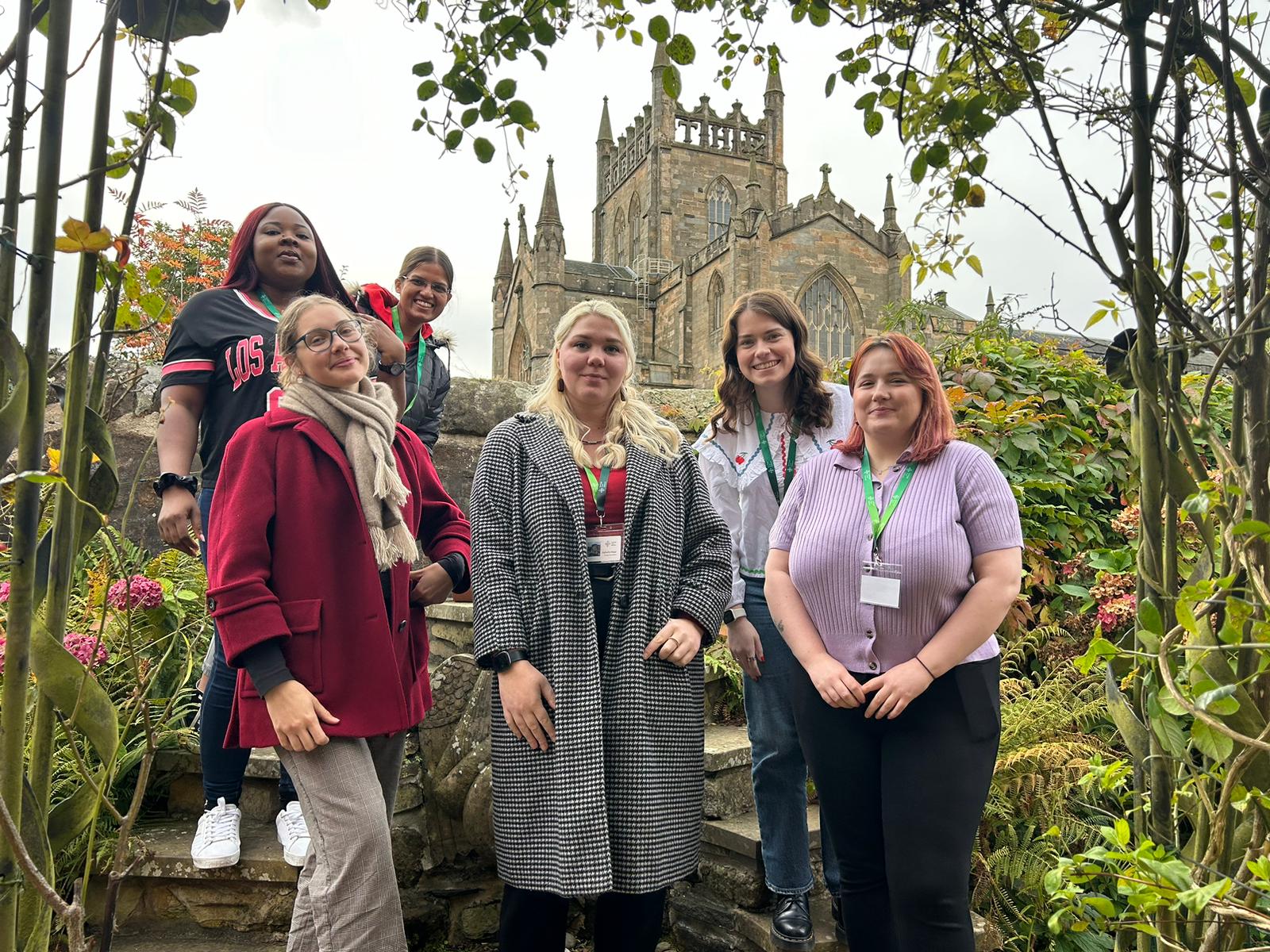 6 young people in a garden, smiling and facing the camera in front of Dunfermline Abbey