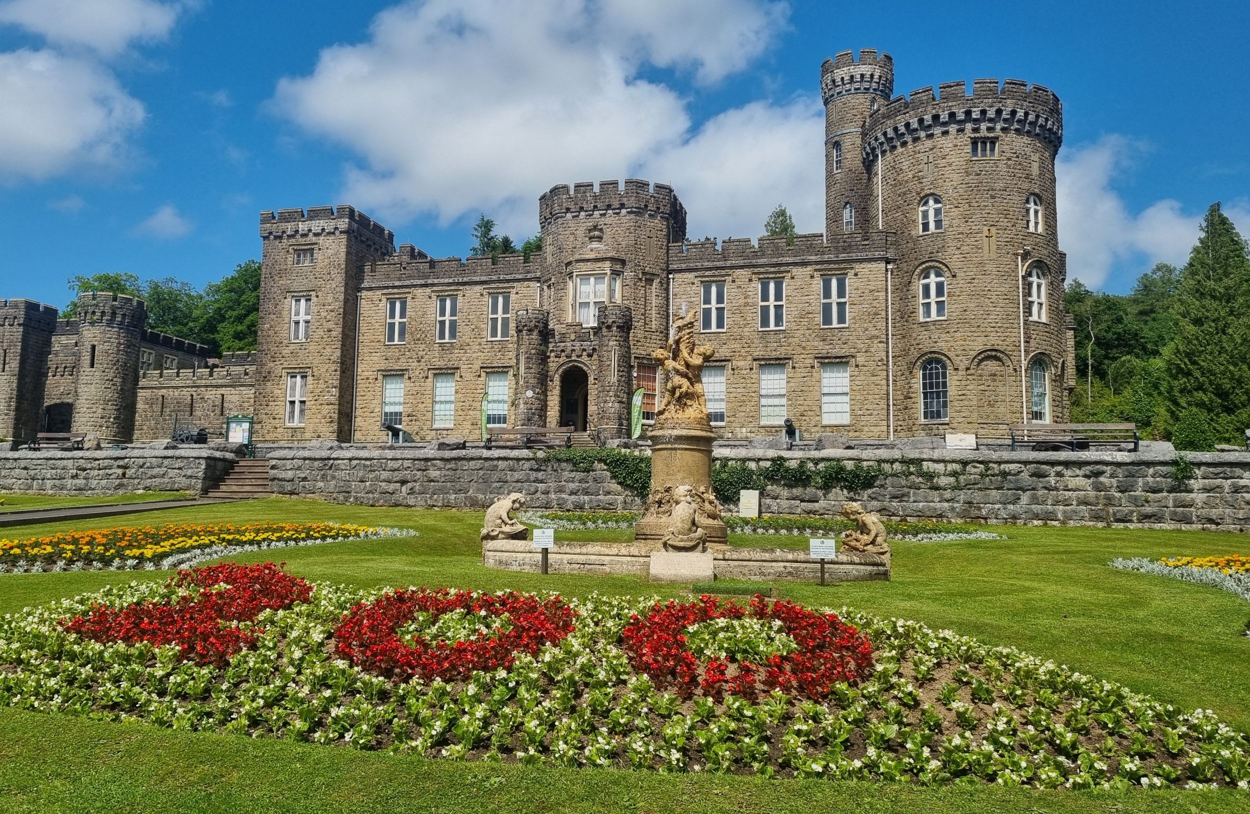 Cyfarthfa Castle with a blue sky. A flowerbed in the foreground with flowers in the shape of 200.