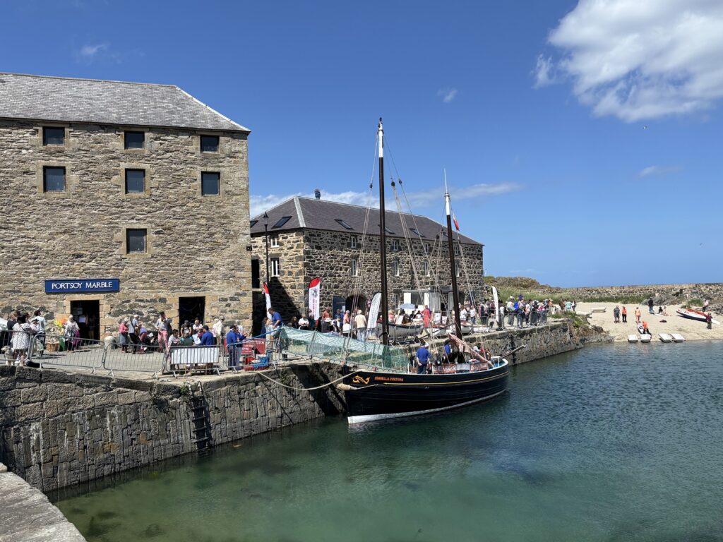 A photograph of Portsoy harbour, with a boat in the water and the Portsoy Marble Warehouse in the background.