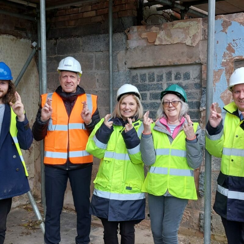 Willow Court Farmhouse Stakeholders stand in a line by the building. They are wearing hard hats and hi-vis and have their fingers crossed.