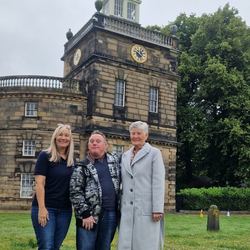 Photograph of Patricia Rollinson, her son Lee and fundraising manager Carol Foster standing in front of the clocktower.