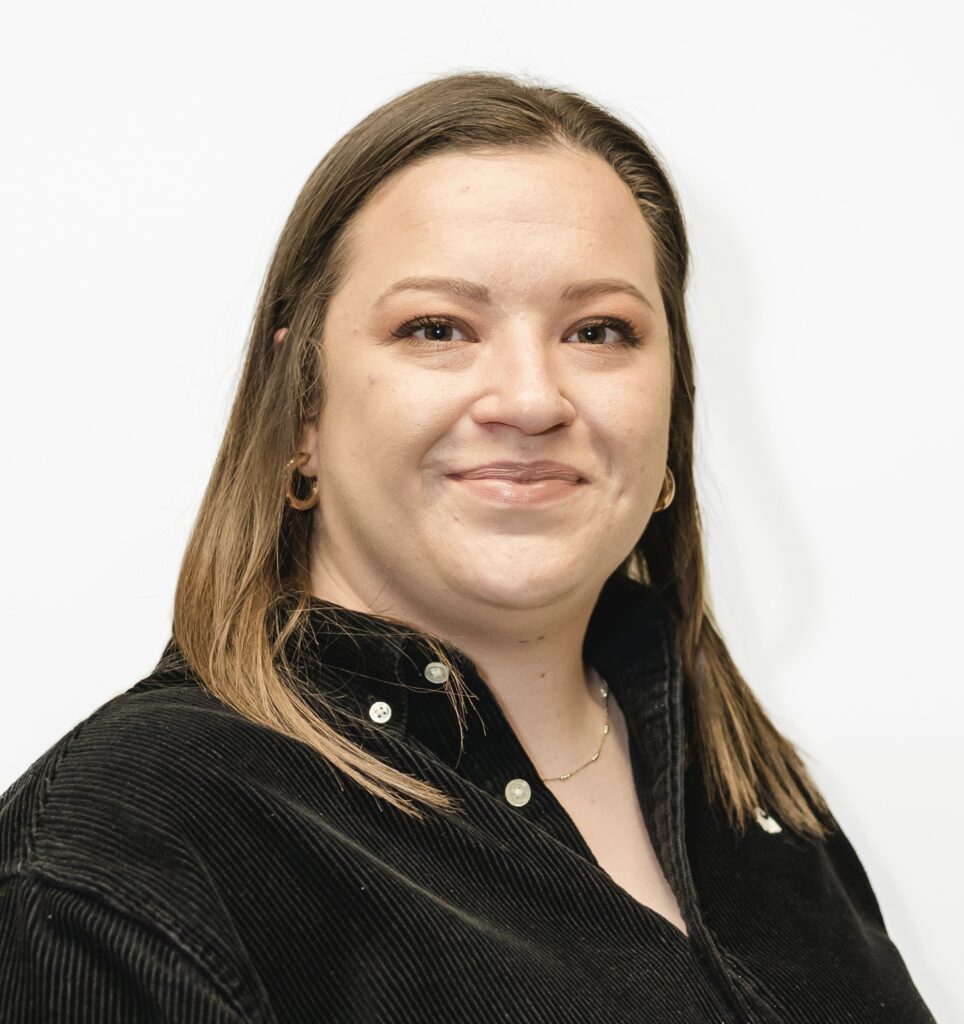 Charlotte facing towards the camera and smiling. She is standing against a white background
