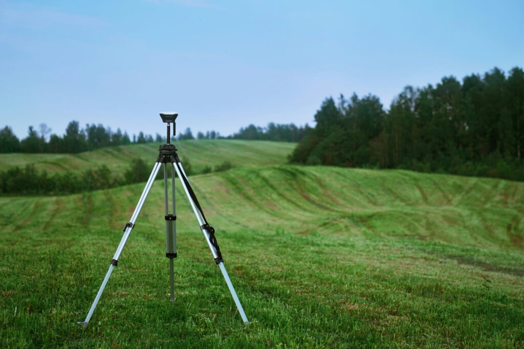 Camera on tripod surrounded by green fields and trees.