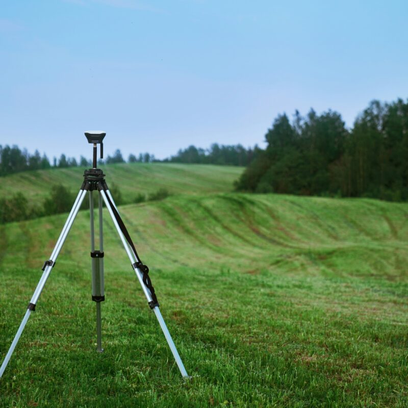 Camera on tripod surrounded by green fields and trees.