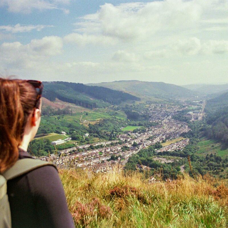 Girl standing on top of a mountain with her back towards the camera. She is looking over the heads of the Rhondda Valleys.