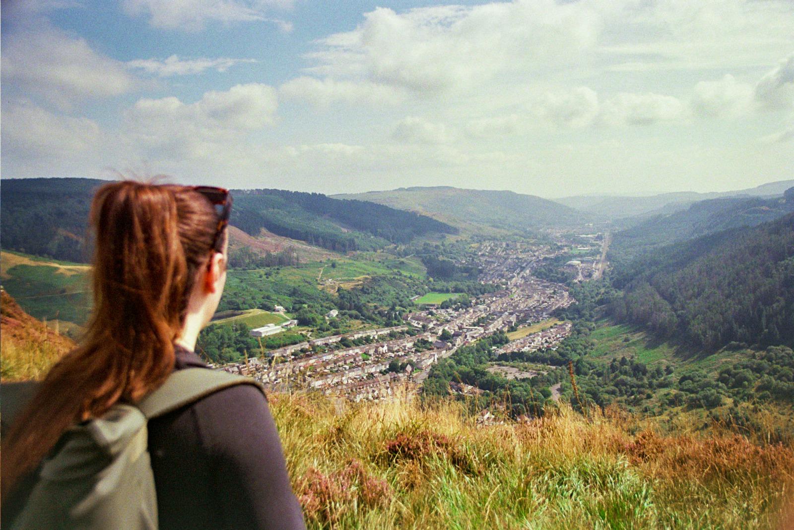 Girl standing on top of a mountain with her back towards the camera. She is looking over the heads of the Rhondda Valleys.