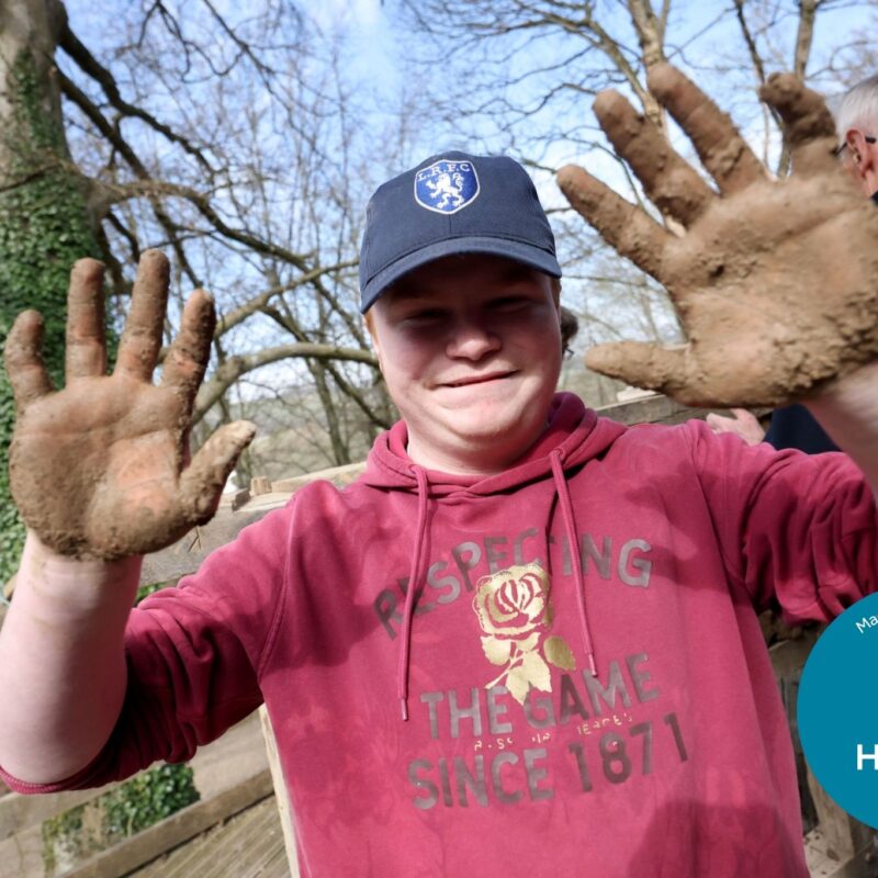 Photograph of a boy in a cap holding up hands covered in wattle and daub.