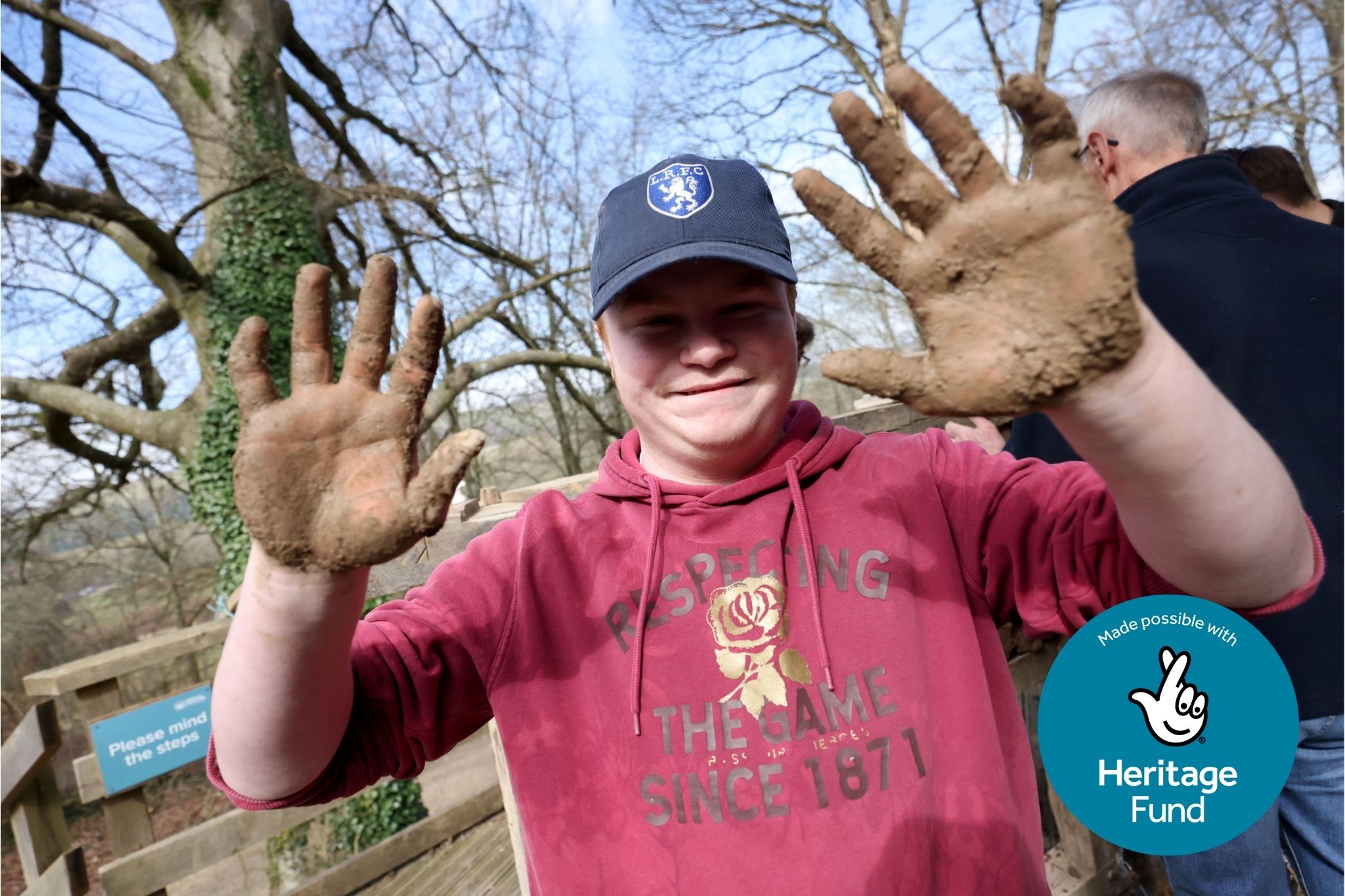 Photograph of a boy in a cap holding up hands covered in wattle and daub.