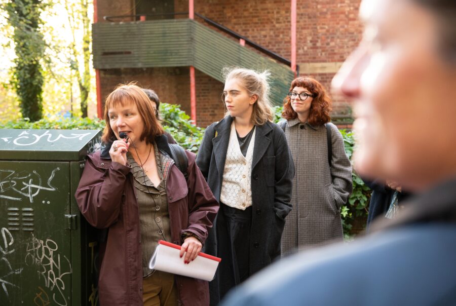 A woman leads a talk outdoors, people look on interested at her and the surroundings.
