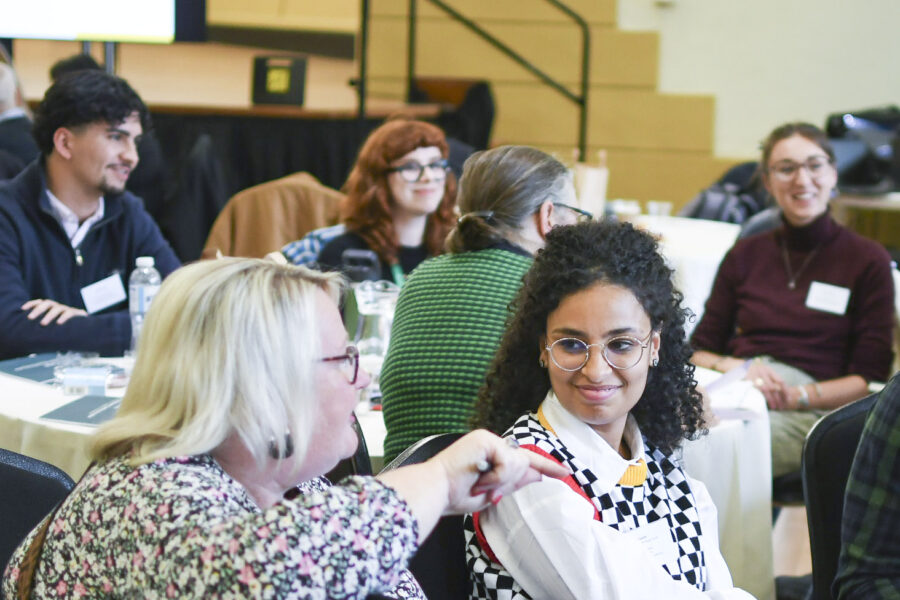 A group of people sit around tables and talk, everyone is smiling and looks relaxed and engaged.
