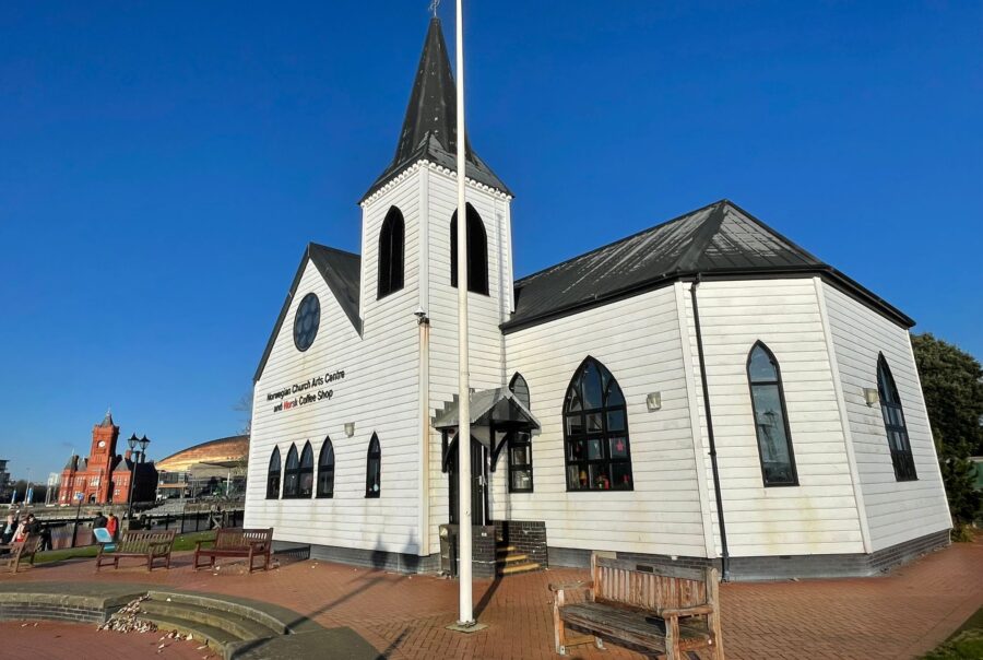 Photograph of the exterior of the Norwegian church in Cardiff Bay, a white, wooden, Scandinavian style church building with arched windows.