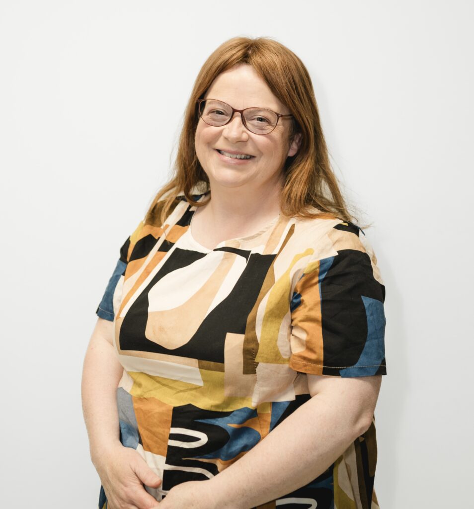 Martina smiling at the camera, wearing a patterned dress and standing against a white background