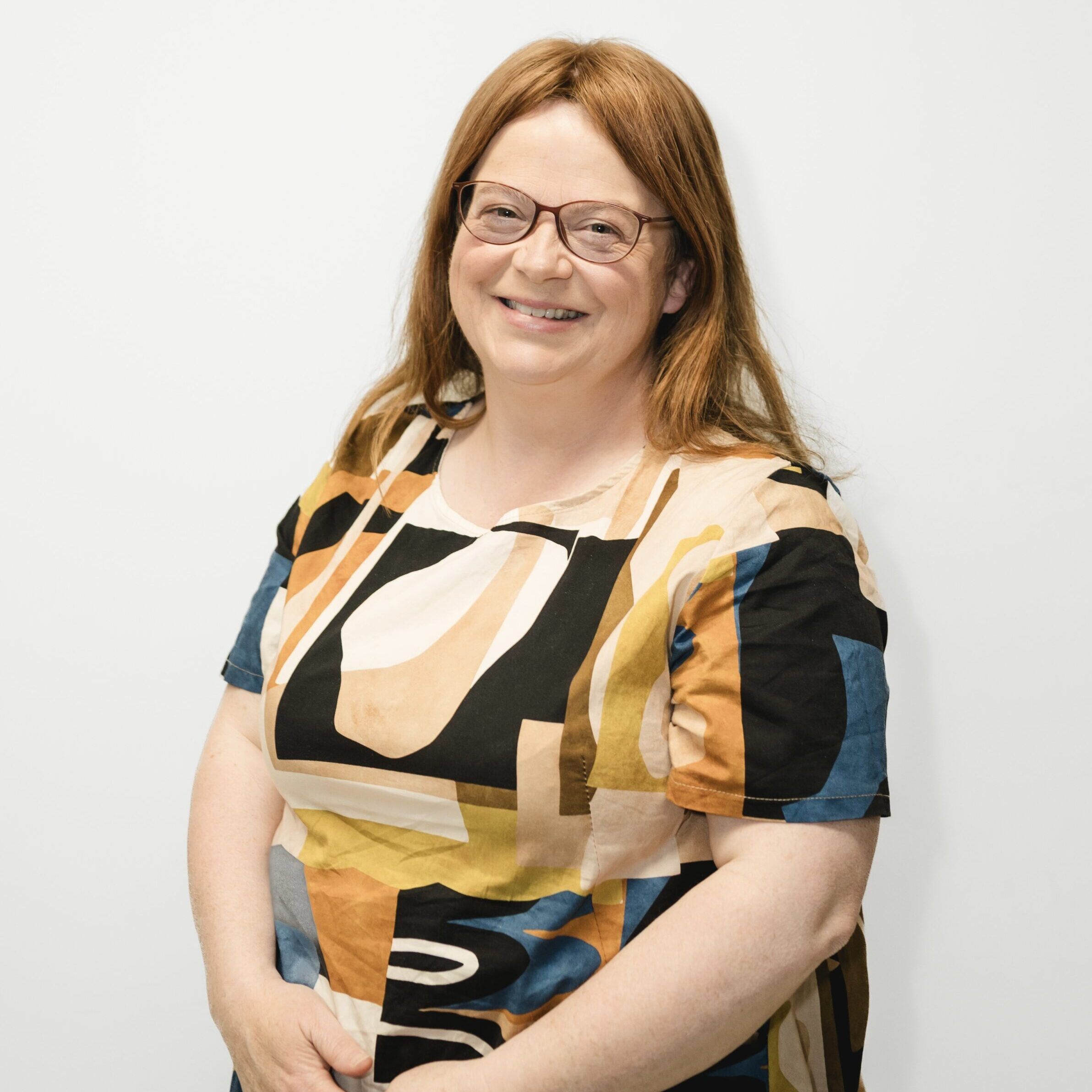 Martina smiling at the camera, wearing a patterned dress and standing against a white background