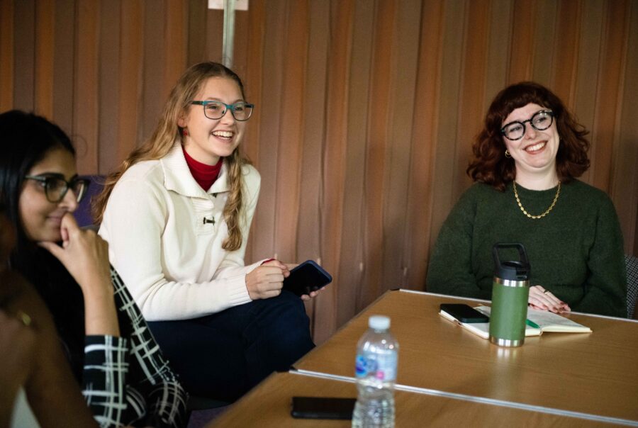 A group of people sat around a table, they are looking at a person speaking out of frame, they are smiling and engaged in what the person is saying.