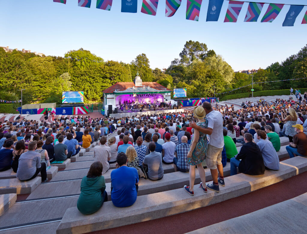 A crowd of people sitting and watching a performance at Kelvingrove Bandstand
