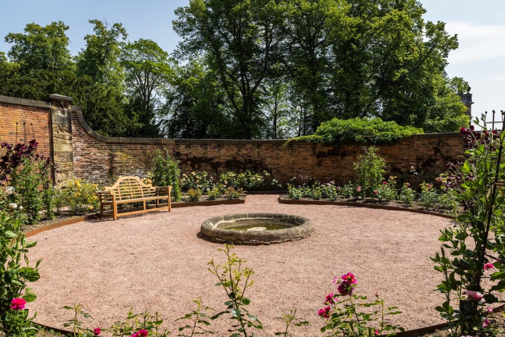 Photograph of the sensory rose garden. It's a circular space with flower beds filled with roses around a circular gravel area which has a stone circle at the centre.