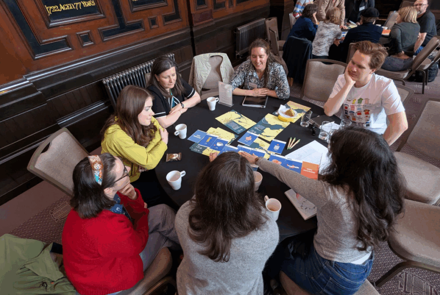 A group of people are gathered around a table smiling and arranging some leaflets