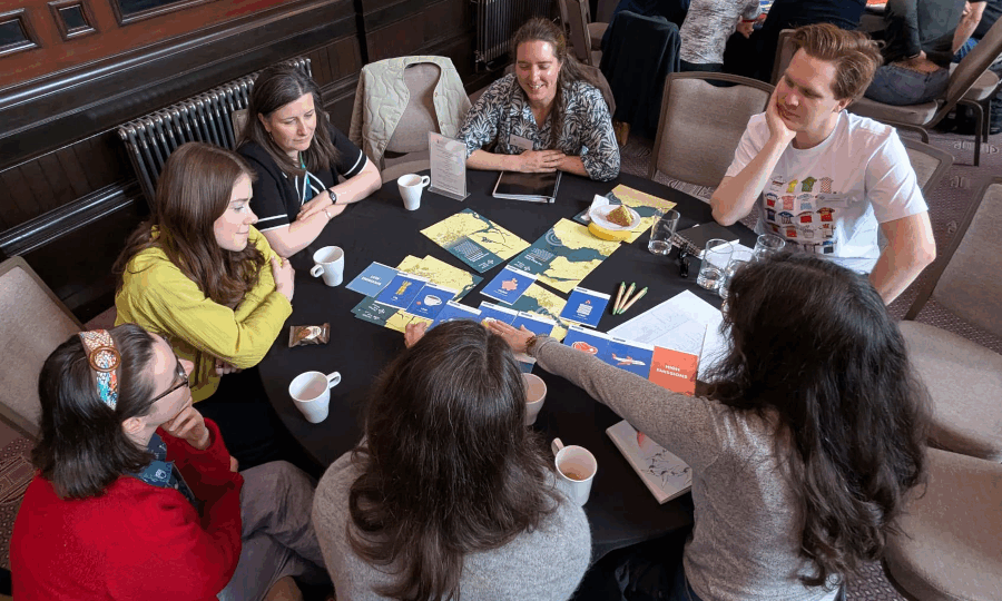 A group of people are gathered around a table smiling and arranging some leaflets