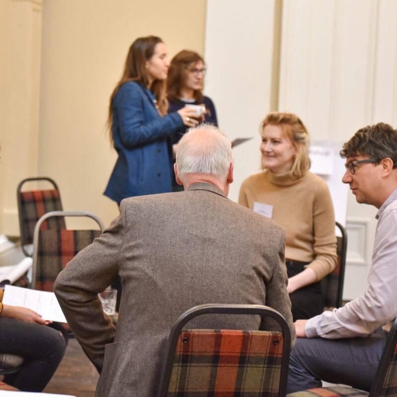 A group of people of mixed ages and genders sit in a small circle of chairs having a discussion.