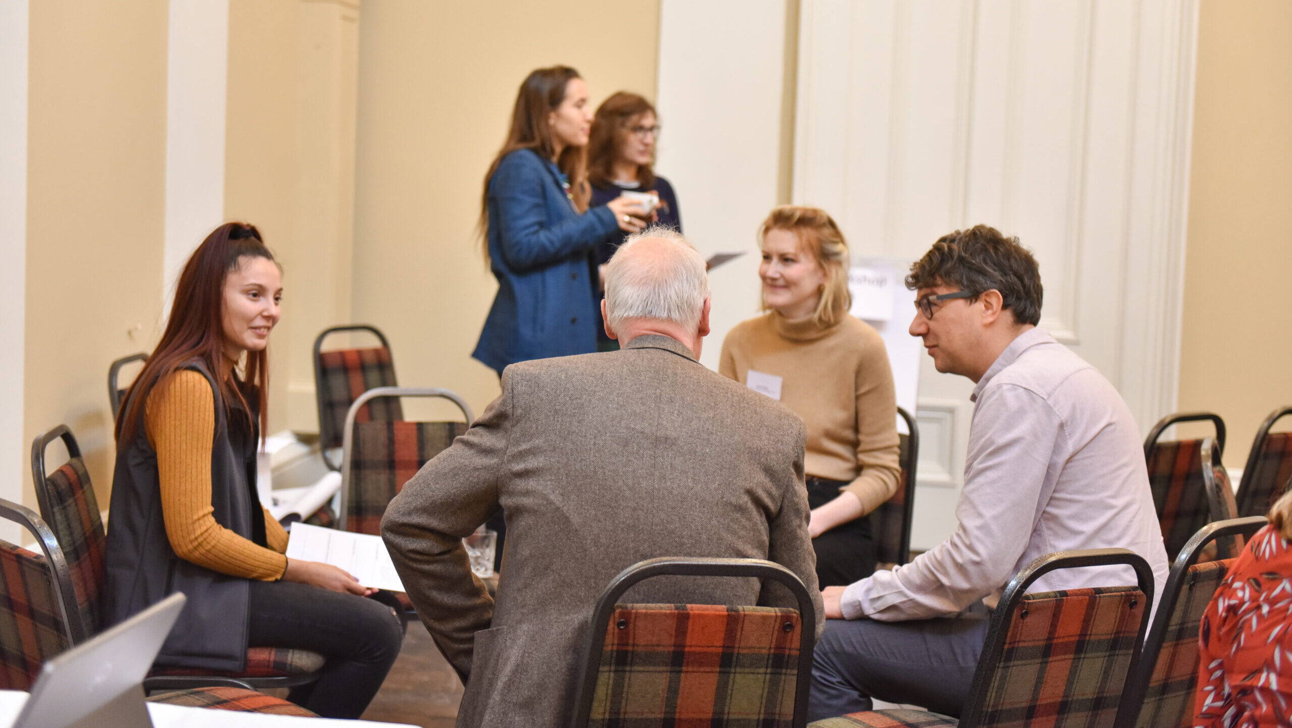 A group of people of mixed ages and genders sit in a small circle of chairs having a discussion.