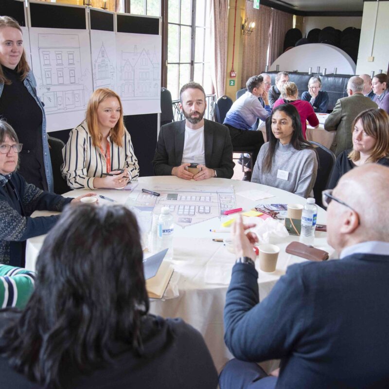 A group of people sit around a table, they are all involved in a discussion and look engaged.