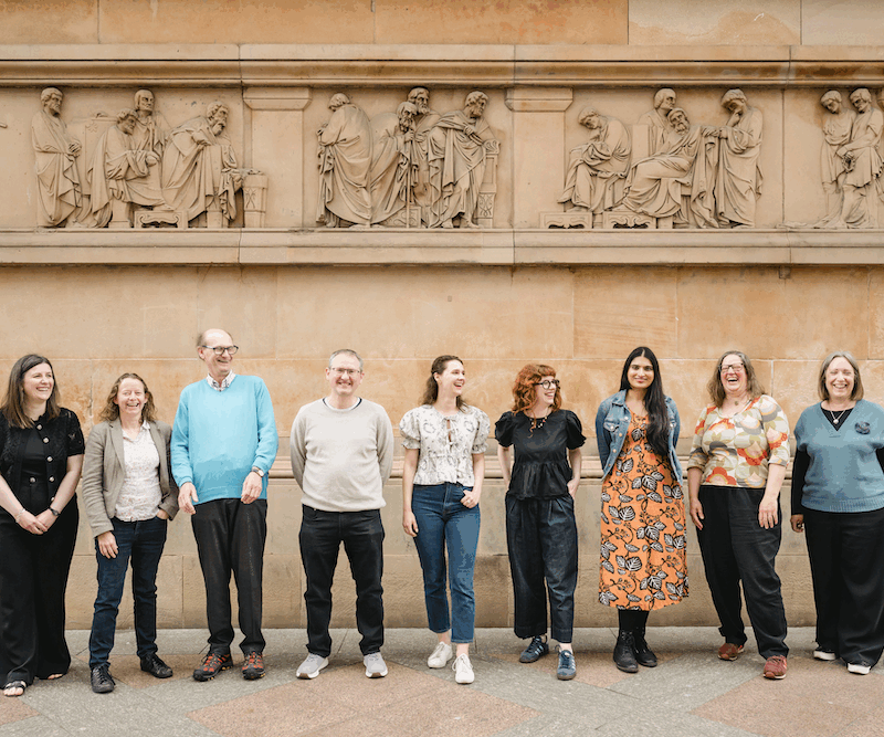 Nine Heritage Network trustees stood in front of a historic stone building with a frieze