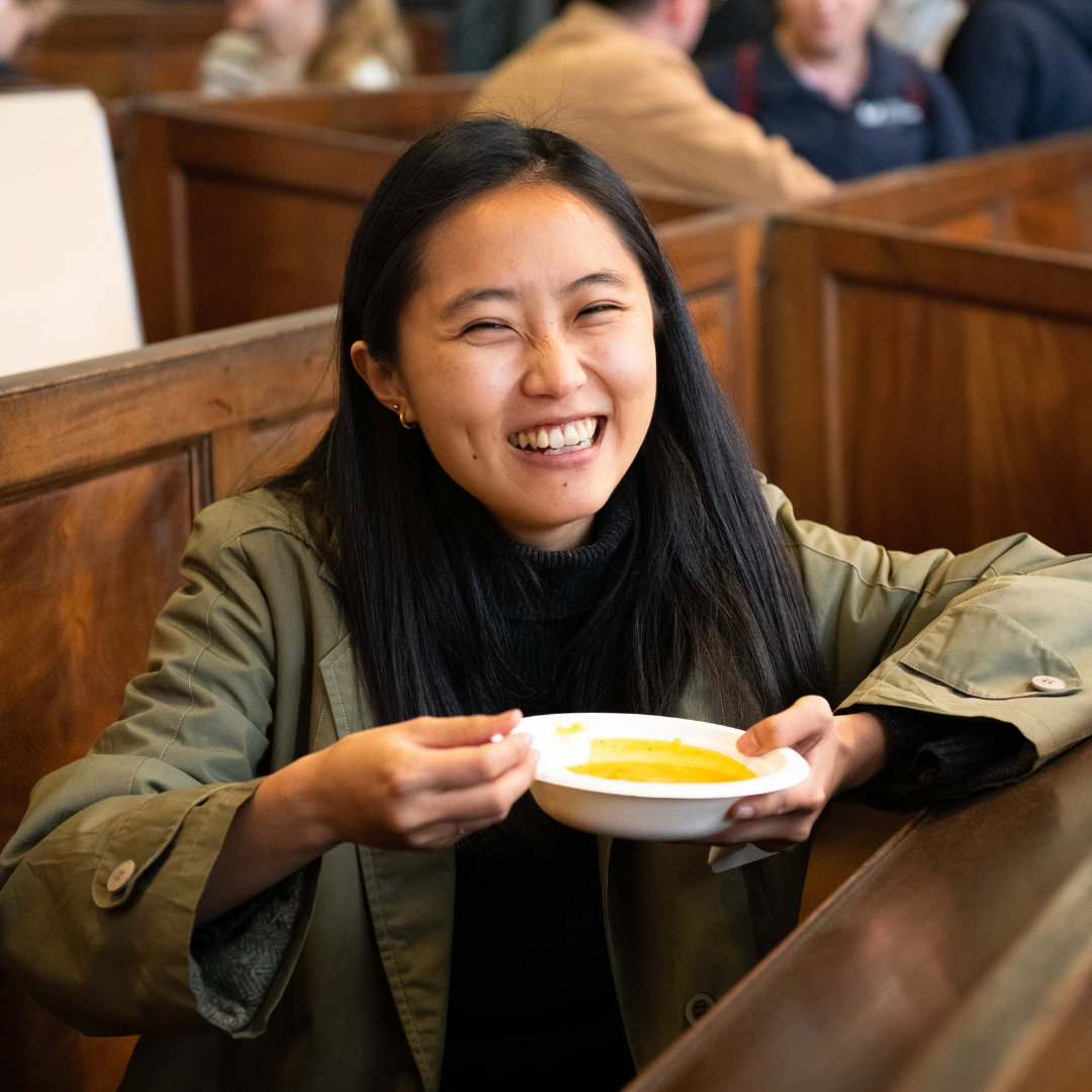 Photograph of a young woman smiling at the camera as she holds a bowl of food