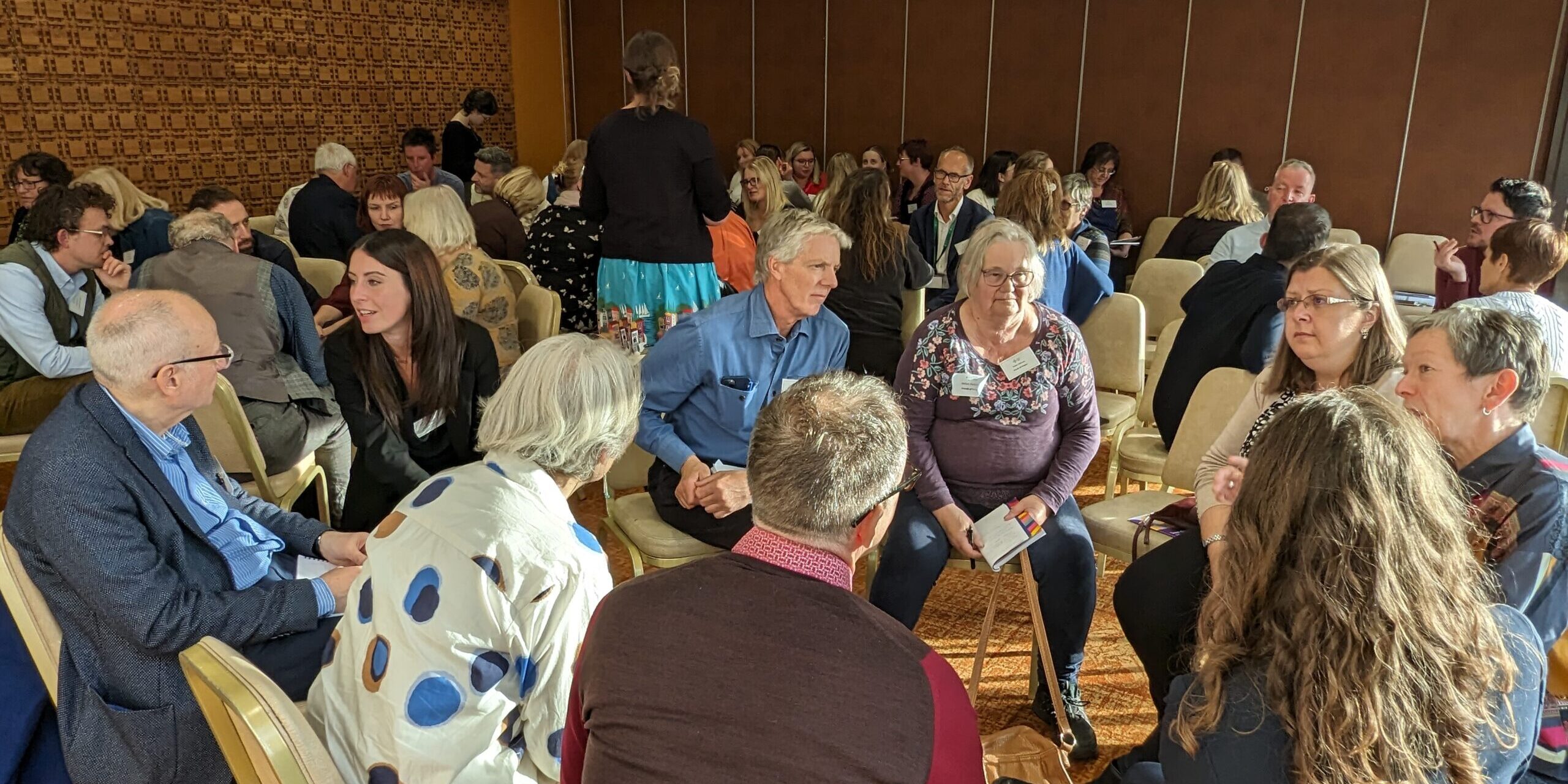 Groups of people sit together in circles at a conference, they are talking and interacting with each other.